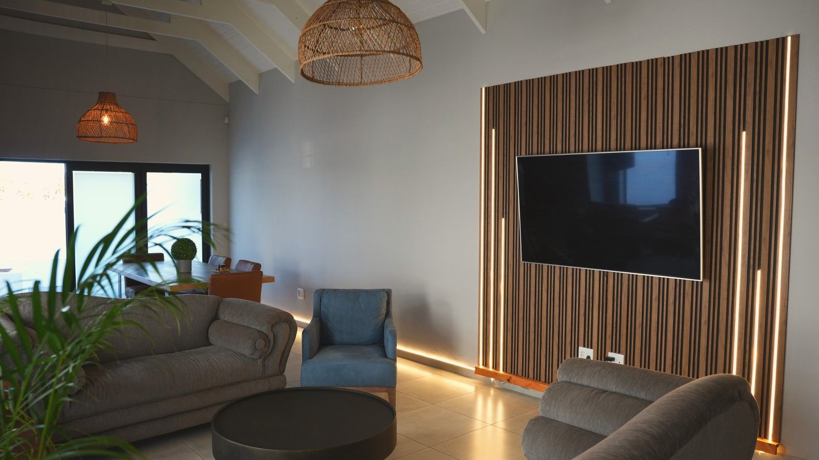 A modern living room with a sofa, armchair, and a television mounted on a wooden panel wall.