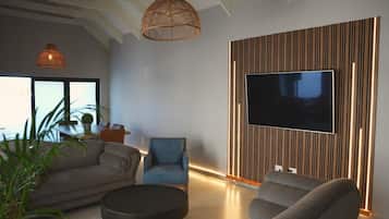 A modern living room with a sofa, armchair, and a television mounted on a wooden panel wall.