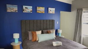Quarto com uma cama grande, cabeceira e quatro quadros pendurados na parede.
