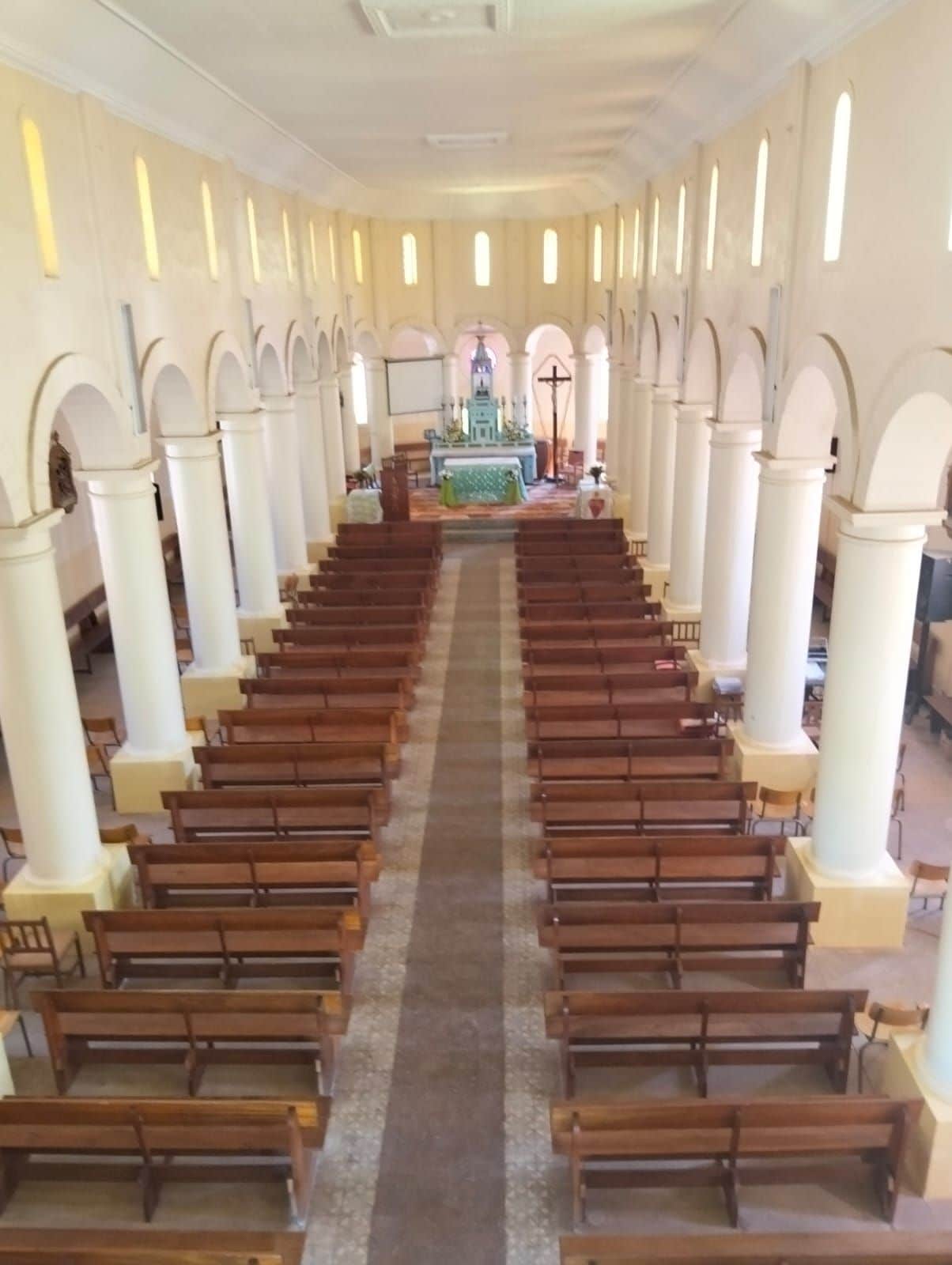 Interior de iglesia con hileras de bancas de madera y un altar central.