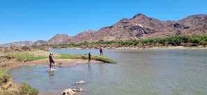 Un río con gente de pie en el agua, rodeado de montañas y vegetación escasa.