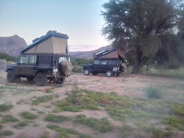 Two vehicles parked in a natural setting with mountains in the background.