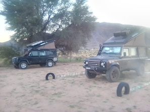 Two off-road vehicles parked in a sandy area with trees in the background.