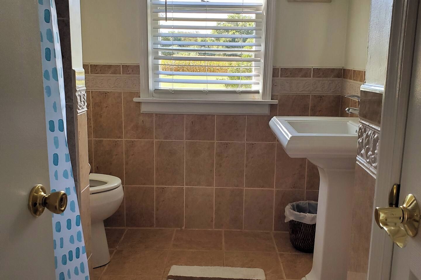 Une salle de bain avec des toilettes, un lavabo et une fenêtre avec des stores.