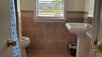 Une salle de bain avec des toilettes, un lavabo et une fenêtre avec des stores.