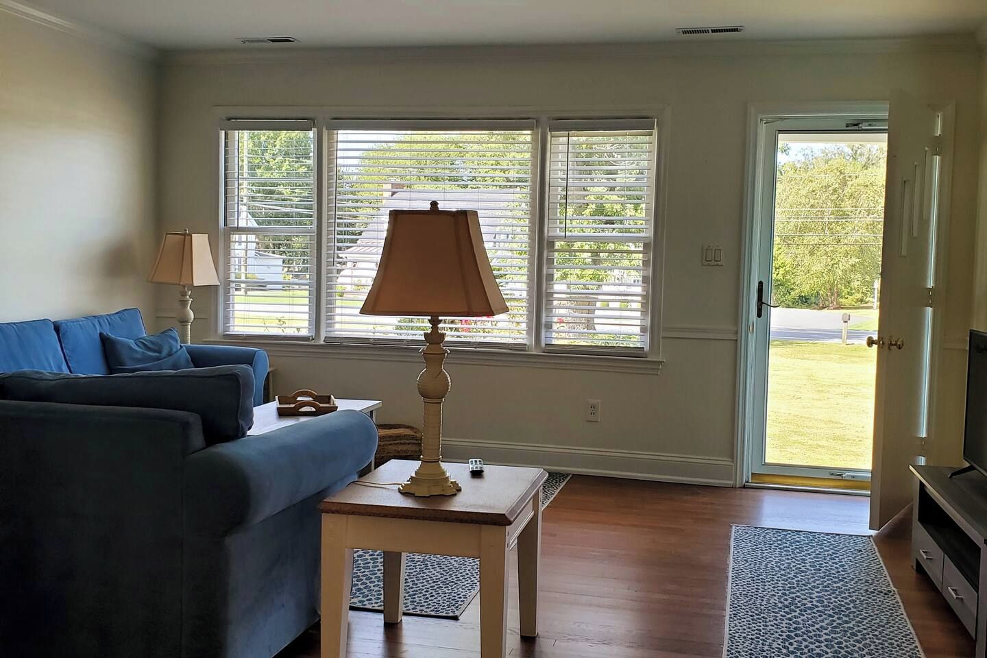 A living room with a sofa, a lamp, a television, and a window with blinds.
