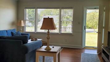 A living room with a sofa, a lamp, a television, and a window with blinds.