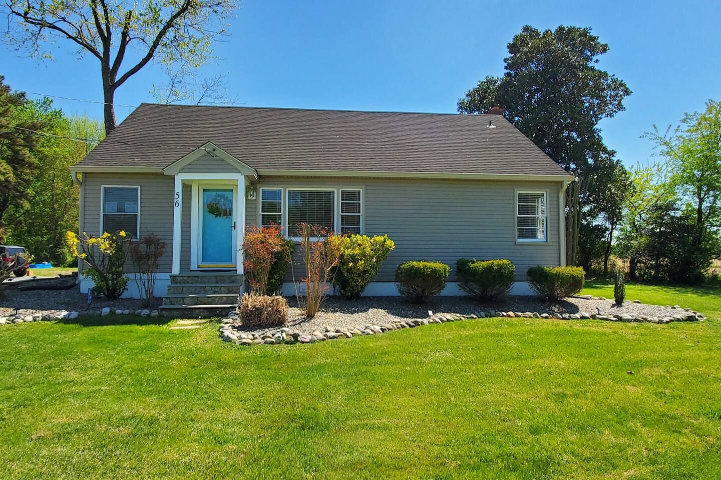 A single-story house with a front porch, a small garden with various shrubs and a lawn.