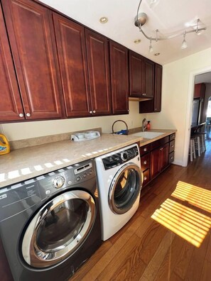 A laundry area with a front-loading washer and dryer, wooden cabinets, and a countertop with a soap dispenser.