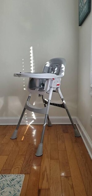 A high chair with a tray table in a room with wooden flooring and a white wall.