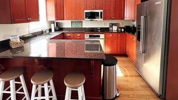 A kitchen with wooden cabinets, a stainless steel refrigerator, a microwave, and a granite countertop.