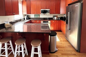 Una cocina con armarios de madera, un refrigerador de acero inoxidable, un microondas y una encimera de granito.