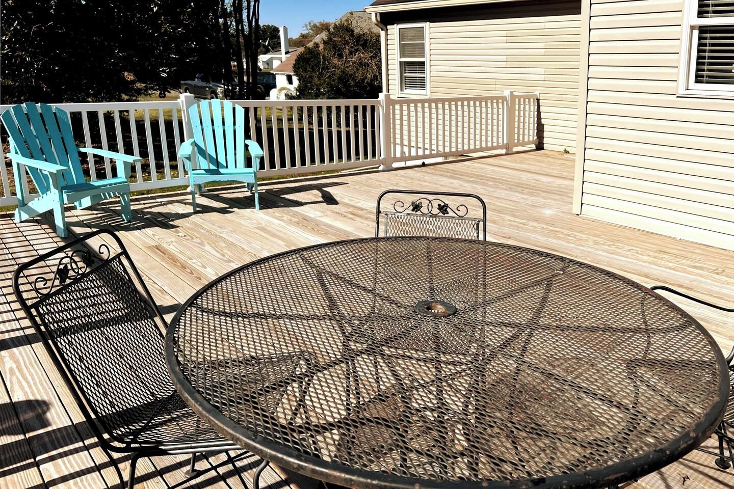 A deck with a round metal table and chairs, a white fence, and a house in the background.