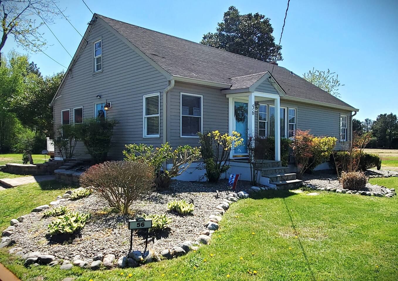 A two-story house with a front porch, a small garden with various plants, and a mailbox.
