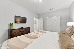 Une chambre à coucher avec un lit, une commode, un téléviseur fixé au mur et une porte.