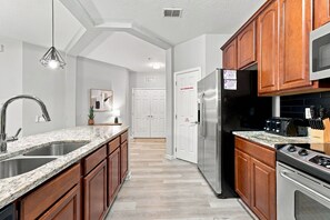 A modern kitchen with granite countertops, stainless steel appliances, and wooden cabinets. - 3BR at Vista Cay, where Comfort meets Convenience (Orlando)