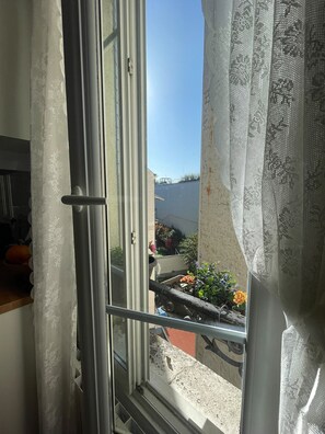 A window with a view of a balcony with plants and a body of water. - PAOLO'S CHARMING APARTMENT (Puteaux)