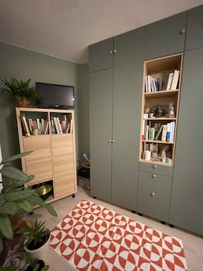 A room with a green wardrobe, a wooden cabinet with books, and a patterned rug. - PAOLO'S CHARMING APARTMENT (Puteaux)