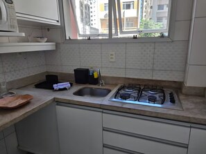A kitchen with a gas stove, a sink, and a window overlooking a residential area. - Studio in downtown Florianópolis, 2 blocks from Trapiche and Av. North Beach (Florianópolis)