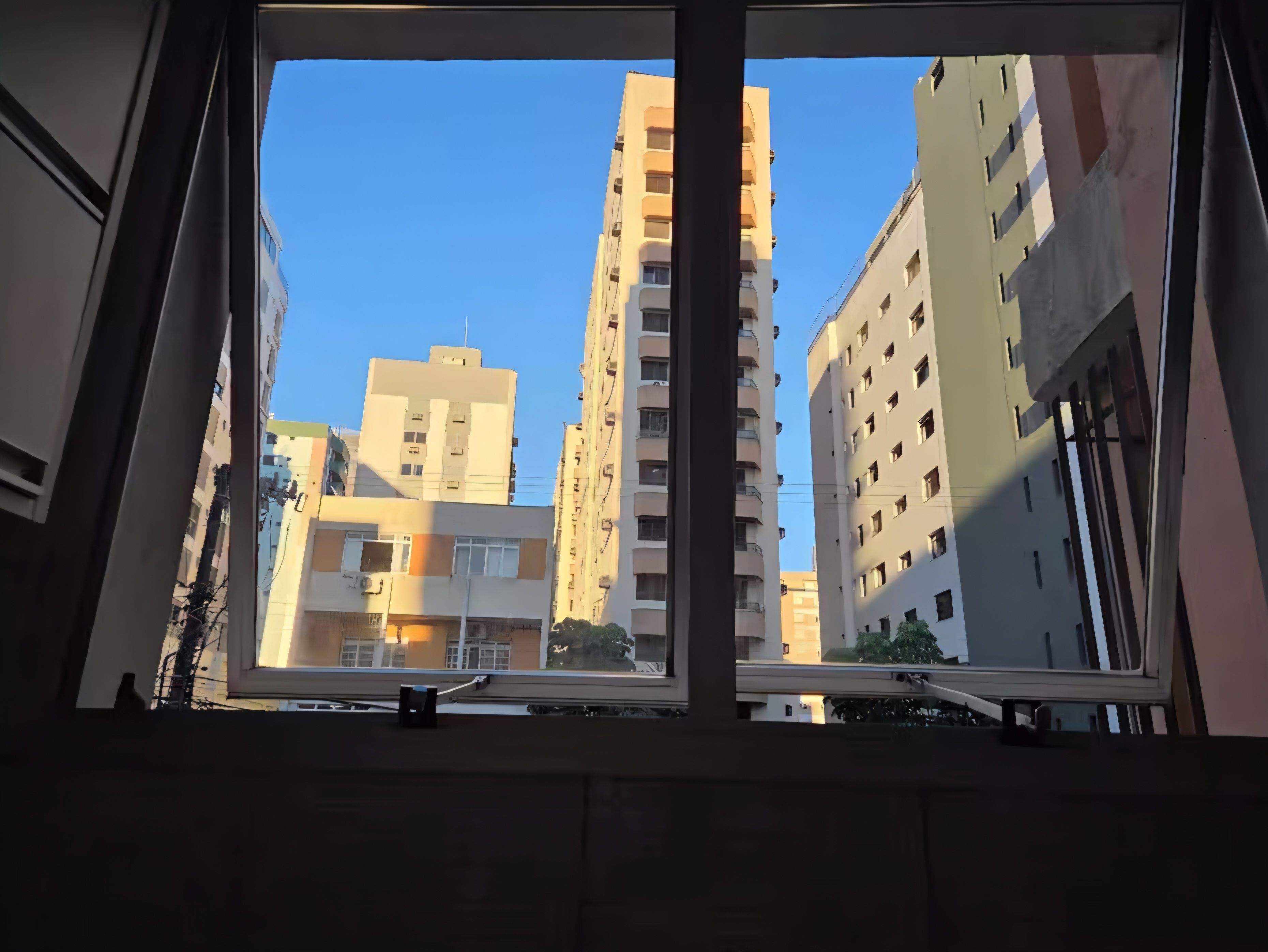 A view through a window of tall residential buildings, with a clear sky visible.