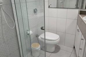 A bathroom with a toilet, a glass shower enclosure, and a toilet paper holder. - Studio in downtown Florianópolis, 2 blocks from Trapiche and Av. North Beach (Florianópolis)
