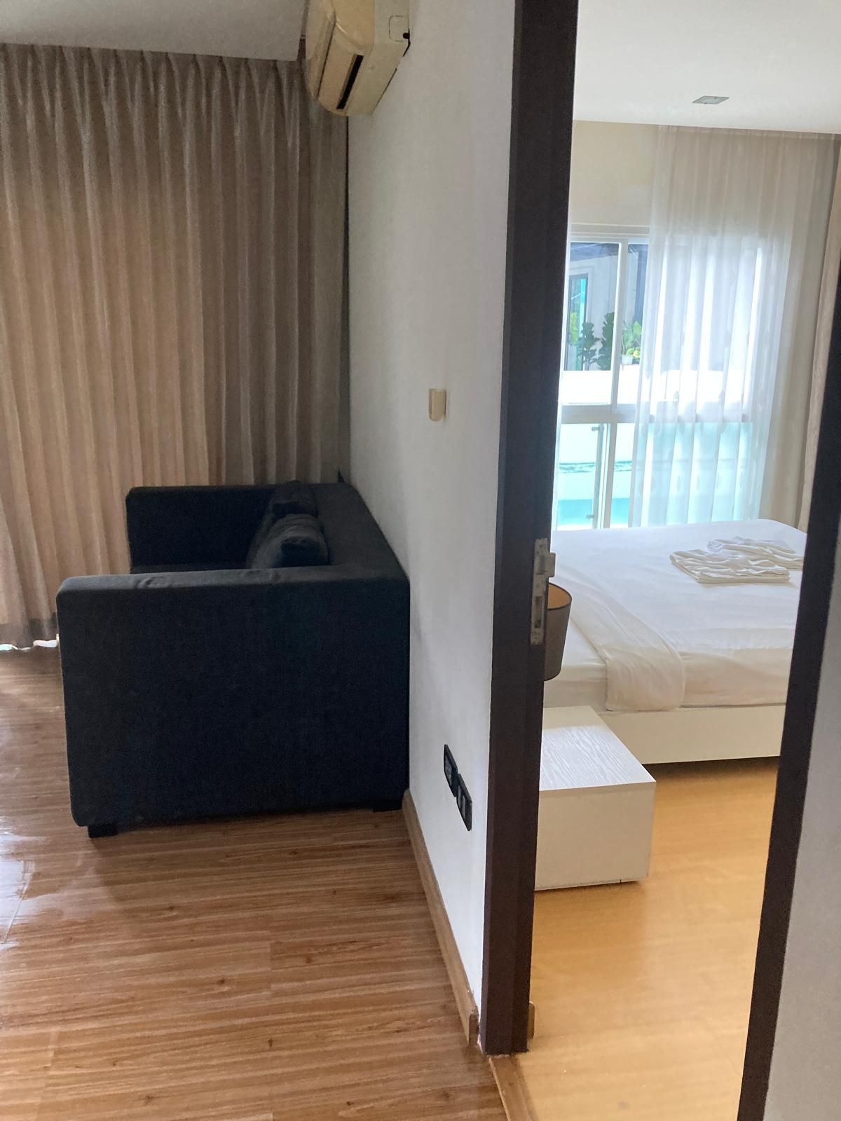 A hotel room with a bed, a sofa, a window with curtains, and a view of the outdoors.