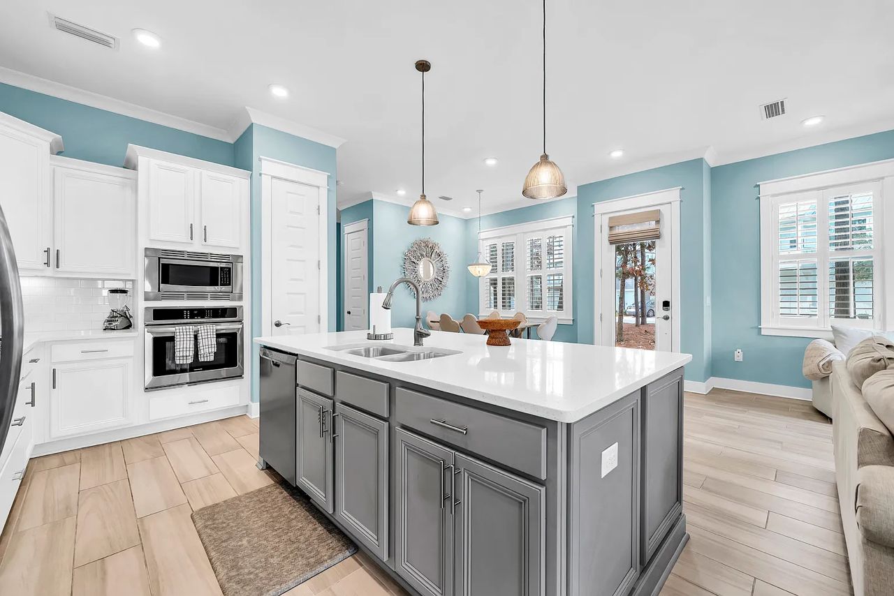 A kitchen with white cabinets, a large island, stainless steel appliances, and pendant lighting.