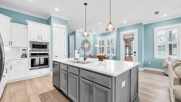 A kitchen with white cabinets, a large island, stainless steel appliances, and pendant lighting.