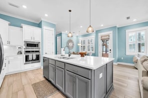 A kitchen with white cabinets, a large island, stainless steel appliances, and pendant lighting.