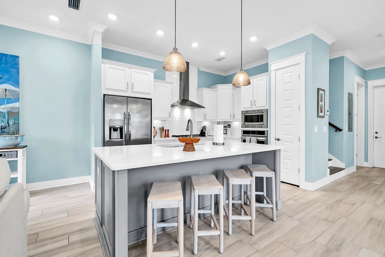 A modern kitchen with white cabinets, a large island with stools, stainless steel appliances, and pendant lighting.