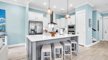 A modern kitchen with white cabinets, a large island with stools, stainless steel appliances, and pendant lighting.