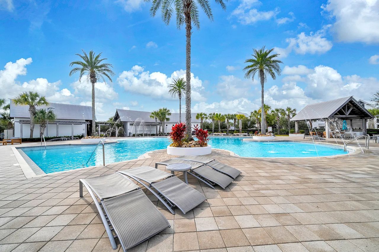 Un espace piscine avec des chaises longues, des palmiers et un ciel dégagé.
