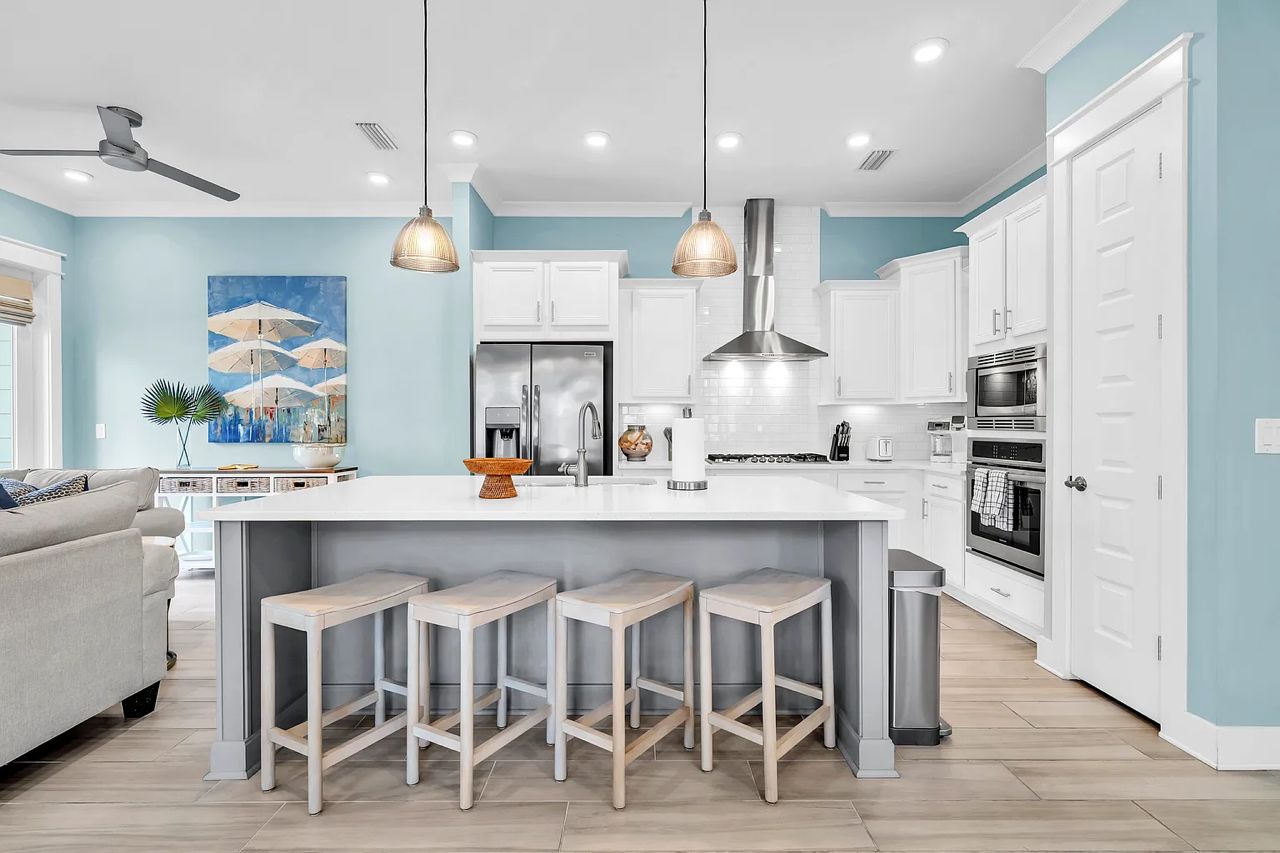 Una cocina moderna con armarios blancos, una isla central con taburetes, iluminación colgante y un ventilador de techo.