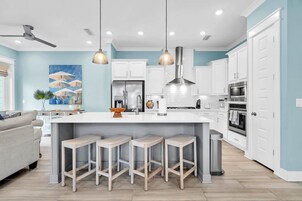 Una cocina moderna con armarios blancos, una isla central con taburetes, iluminación colgante y un ventilador de techo.