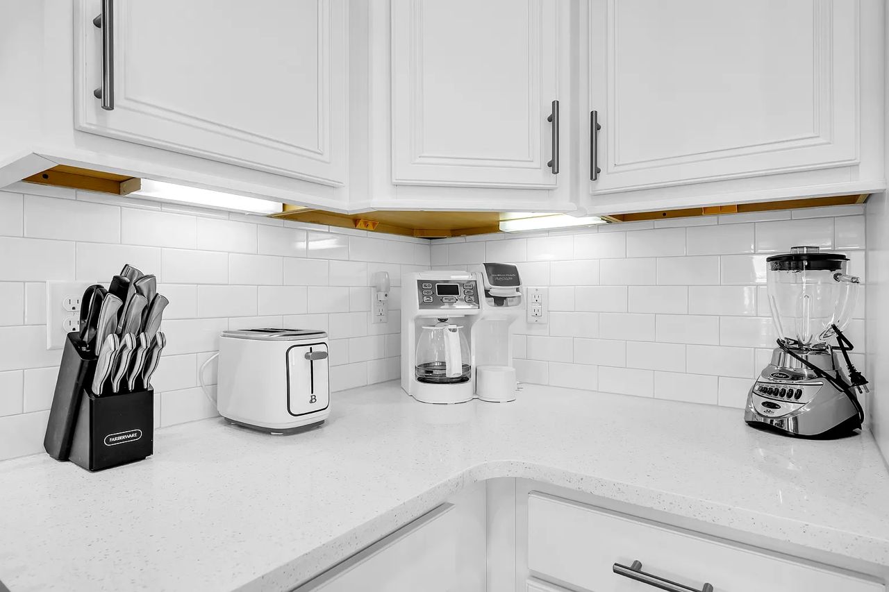 A kitchen with white cabinets, a toaster, a coffee maker, and a blender on the countertop.