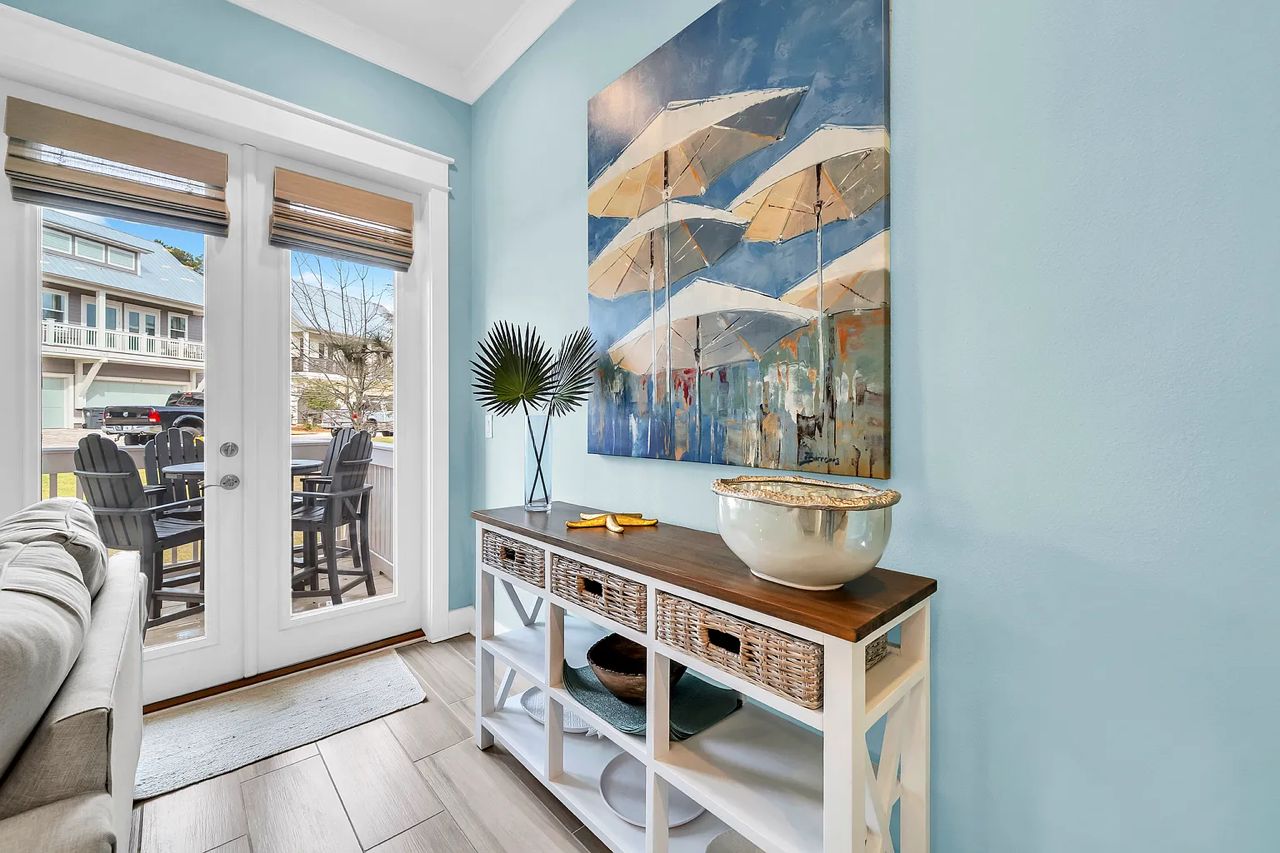 A room with a sliding glass door leading to an outdoor patio, a dining table with chairs, a white console table with baskets, and a large abstract painting on the wall.