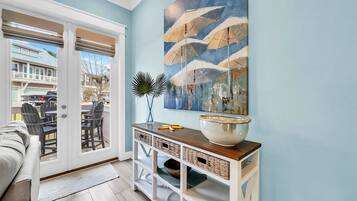 A room with a sliding glass door leading to an outdoor patio, a dining table with chairs, a white console table with baskets, and a large abstract painting on the wall.