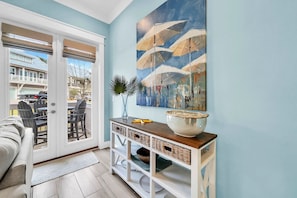 A room with a sliding glass door leading to an outdoor patio, a dining table with chairs, a white console table with baskets, and a large abstract painting on the wall.