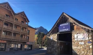 Een traditionele chalets met een bord waarop 'Bienvenue A La Mongie' staat en een stenen gebouw met een bord 'Place des Moulins'.