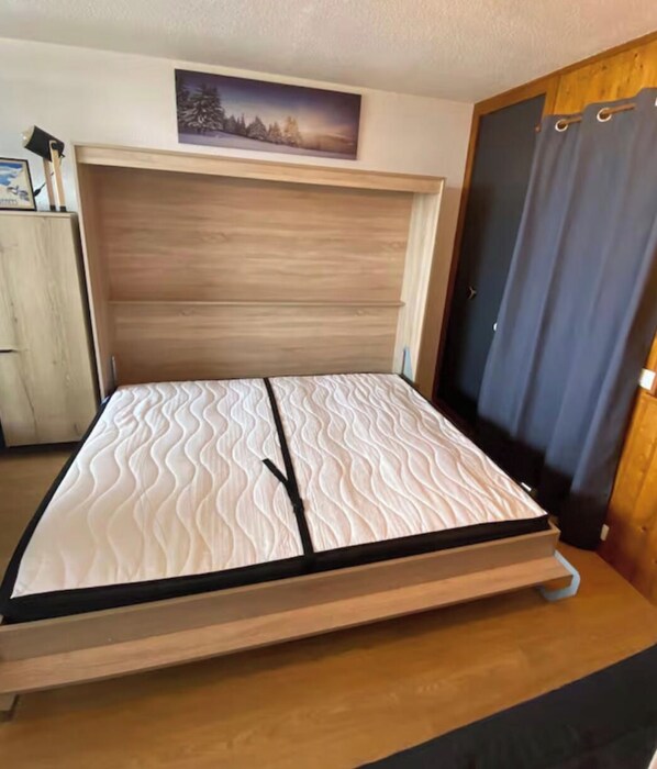 A bed with a wooden headboard, a wall-mounted picture, and a door with curtains. - La Mongie 1800 – At the base of the slopes, balcony, in the heart of the resort – Sleeps 6 (Bagnères-de-Bigorre)