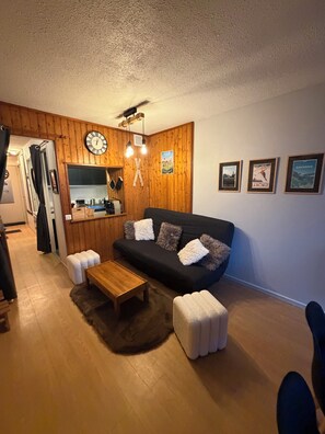 A cozy living room with a wooden floor, a black sofa with fluffy cushions, a wooden coffee table, and a small ottoman. - La Mongie 1800 – At the base of the slopes, balcony, in the heart of the resort – Sleeps 6 (Bagnères-de-Bigorre)