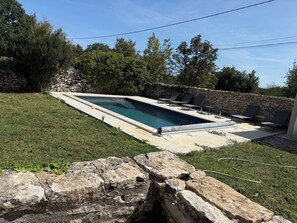 Piscina retangular com muro de pedra e espreguiçadeiras.