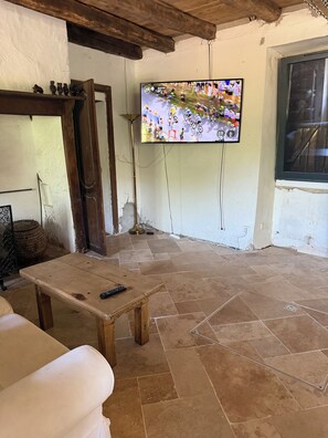 Ein Zimmer mit einem an der Wand befestigten Fernseher, einem Holztisch und einem gefliesten Boden.