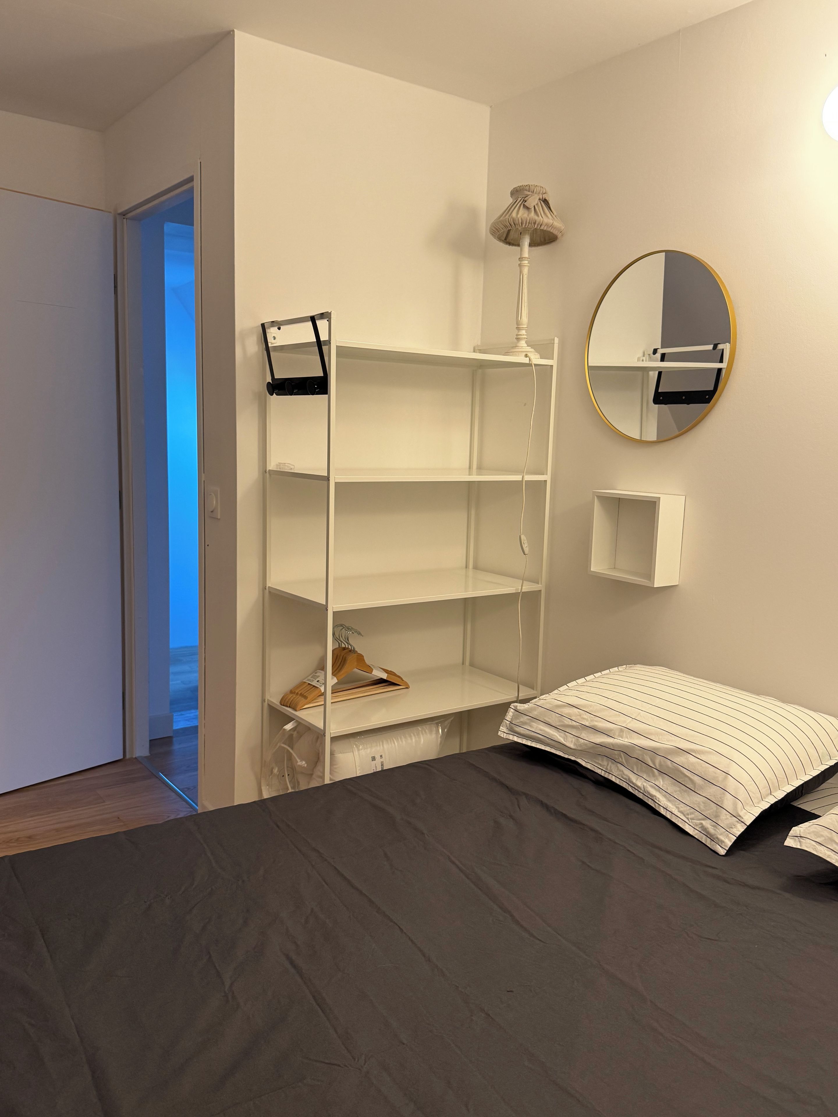 Une chambre à coucher avec un lit, une armoire blanche, un miroir et une porte donnant sur une autre pièce.
