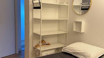 Une chambre à coucher avec un lit, une armoire blanche, un miroir et une porte donnant sur une autre pièce.