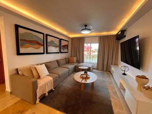 A modern living room with a sectional sofa, a round coffee table, and a flat-screen TV mounted on the wall. - The Amber Haven V. (Samana)