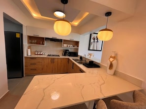 A modern kitchen with marble countertops, wooden cabinets, and pendant lighting. - The Amber Haven V. (Samana)