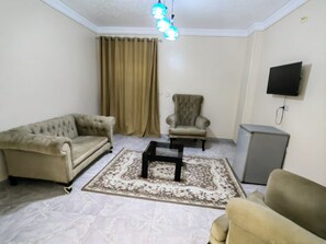 A living room with a sofa, armchair, coffee table, and a television mounted on the wall. - Gem& pyramids front  (Giza)