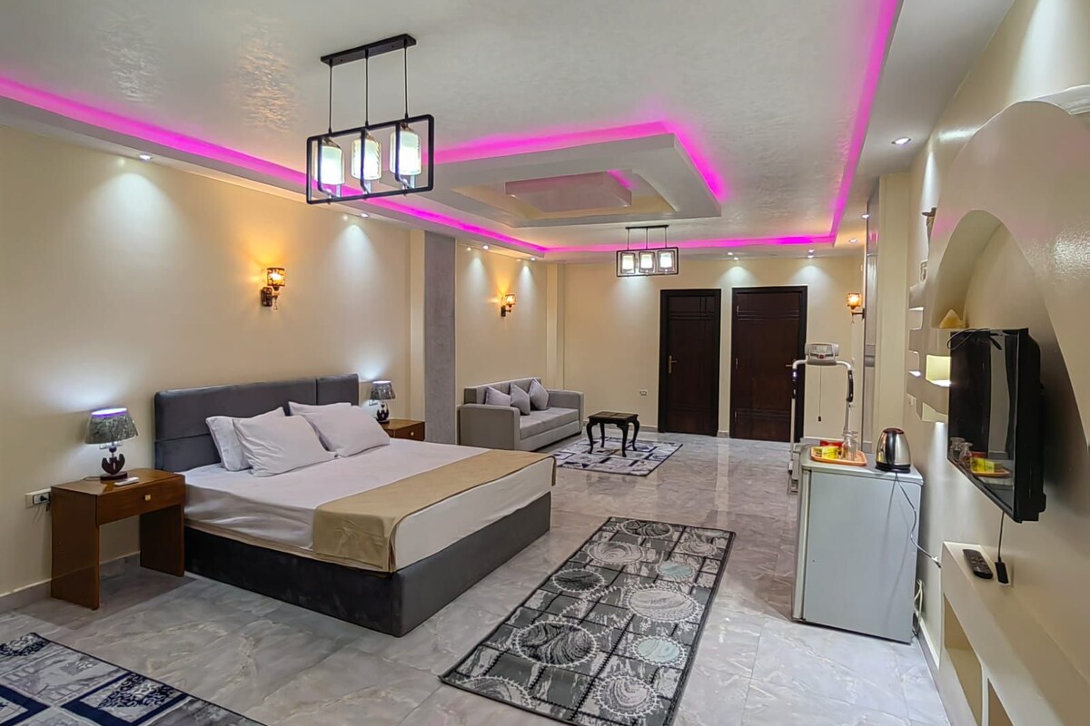 A modern bedroom with a bed, a sofa, a desk, and a television.