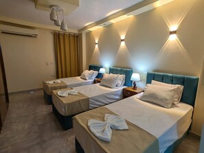 A hotel room with two beds, each with a pillow and a towel, a nightstand with a lamp, and a ceiling-mounted air conditioner. - Gem& pyramids front  (Giza)